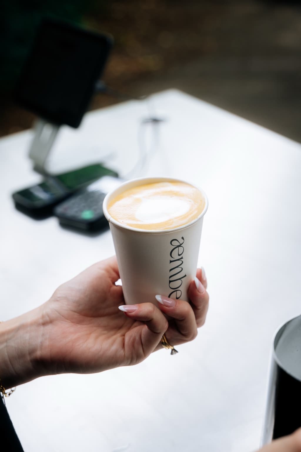 Cappuccino im æmber.-Becher, in einer Hand gehalten